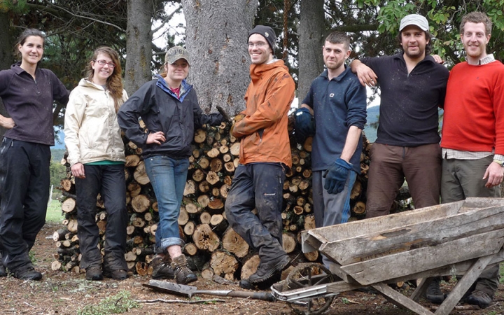 A group of people smile for a photo in front of a stack of wood. 