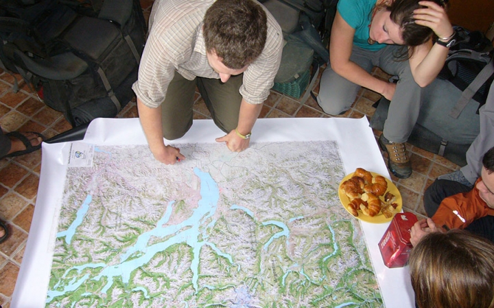 A map is spread out on the floor while a group of people examine it. 
