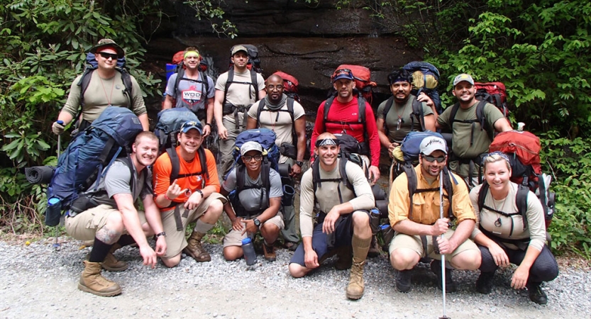 A group of veterans wearing backpacks pose for a photo on an outward bound trip.